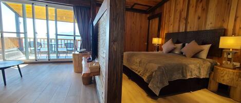 Une chambre à coucher aux murs lambrissés, dotée d’un grand lit, de lampes de chevet et offrant une vue sur l’extérieur grâce à une porte-fenêtre coulissante.