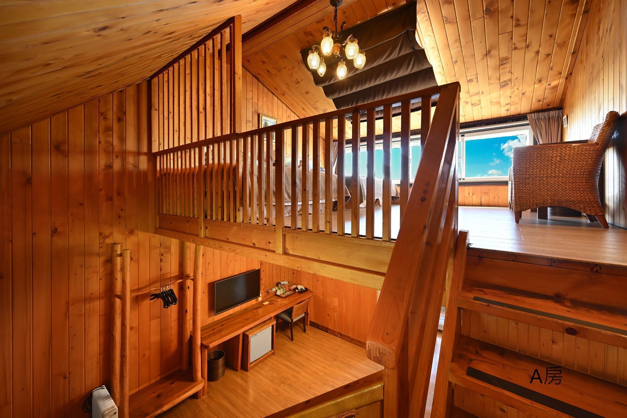Interior de una cabaña de madera con televisión, kitchenette y una silla de mimbre junto a una ventana.