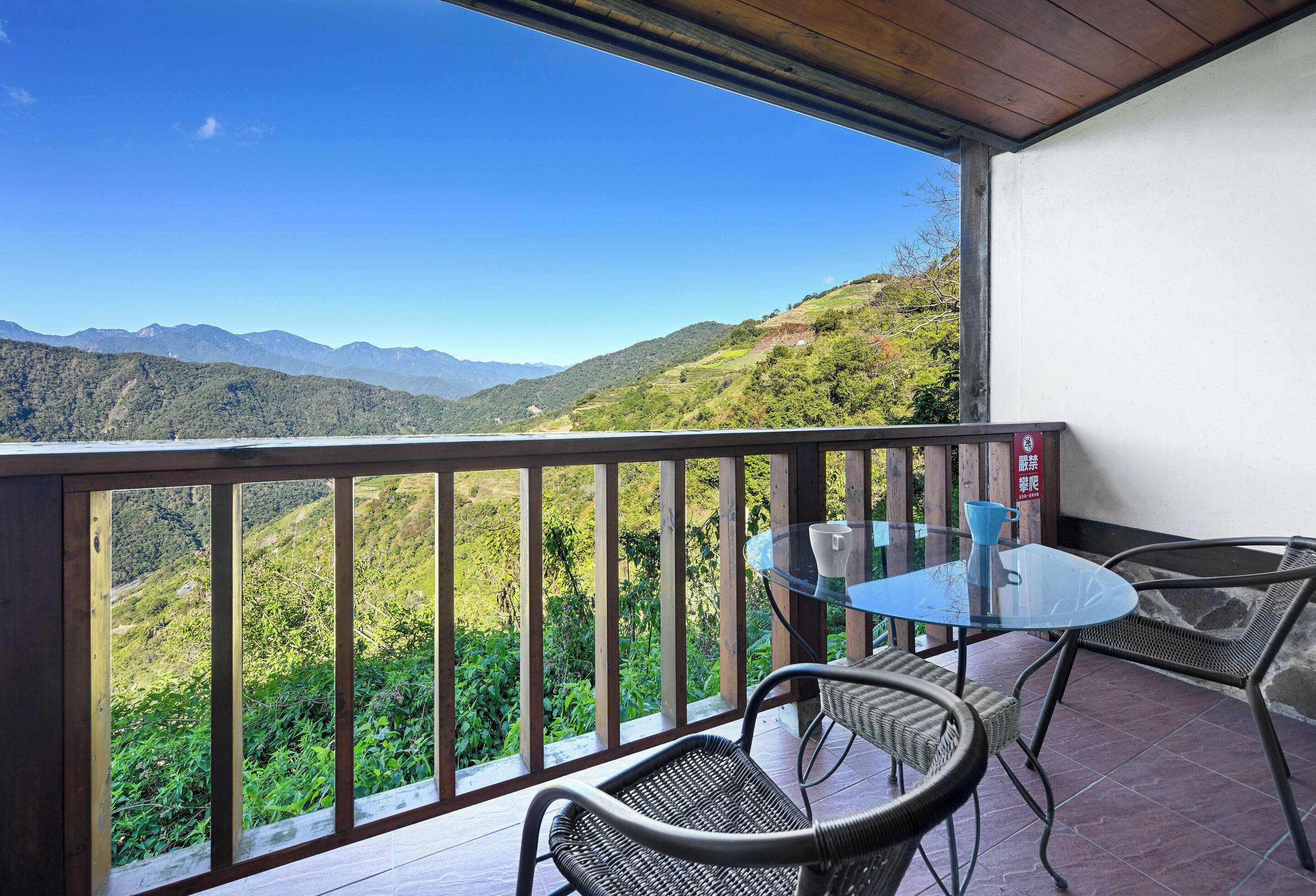 Ein Balkon mit Glastisch und Korbstühlen mit Blick auf eine gebirgige Landschaft.