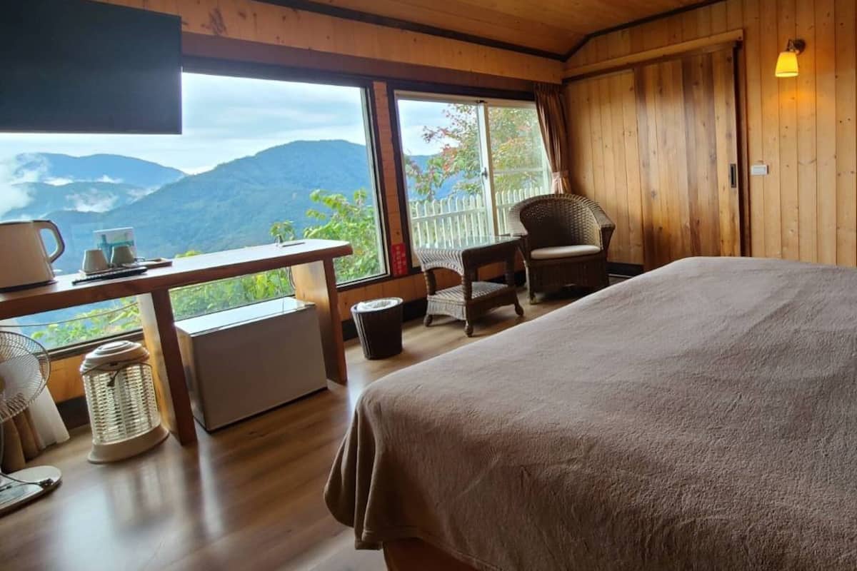 A room with a bed, a desk, a chair, and a large window offering a mountain view.