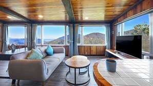 A modern interior with a wooden ceiling, large windows offering mountain views, a sofa, a round table, and a flat-screen TV. - Top Cloud Villa (Ren'ai)