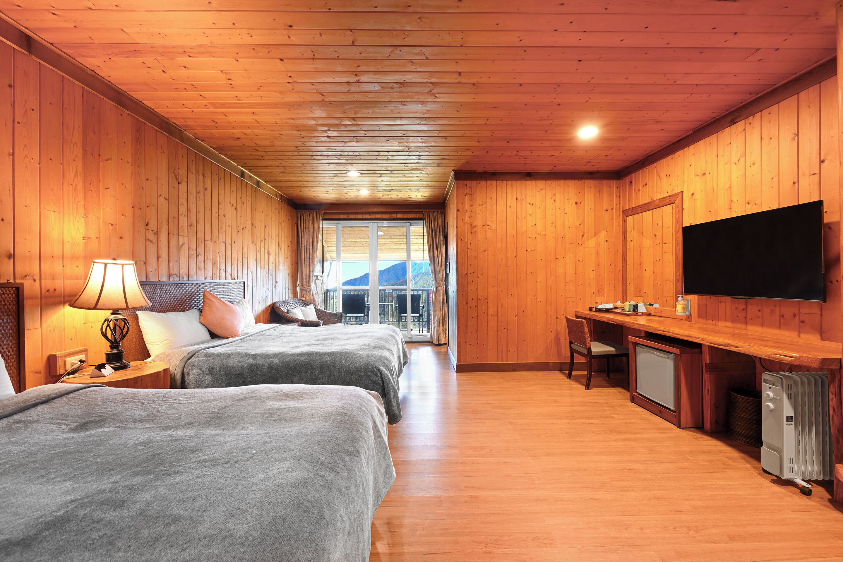 Una habitación con paredes y suelos de madera, dos camas, un escritorio, un televisor y una ventana con vistas a las montañas.