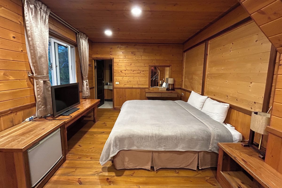 A wooden cabin room with a bed, a TV, and a small desk.