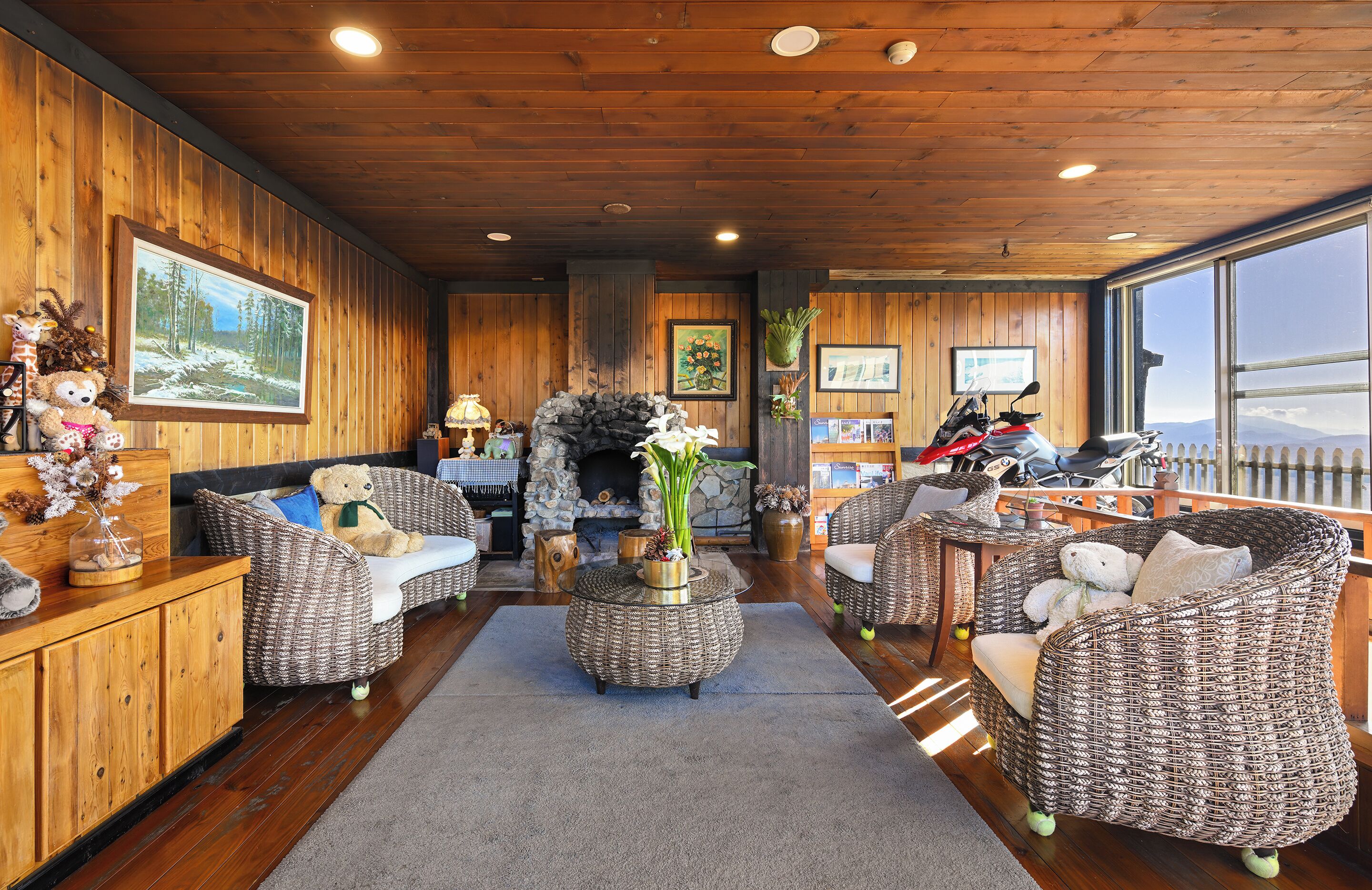 A cozy room with wicker furniture, a stone fireplace, and a large window offering a view.