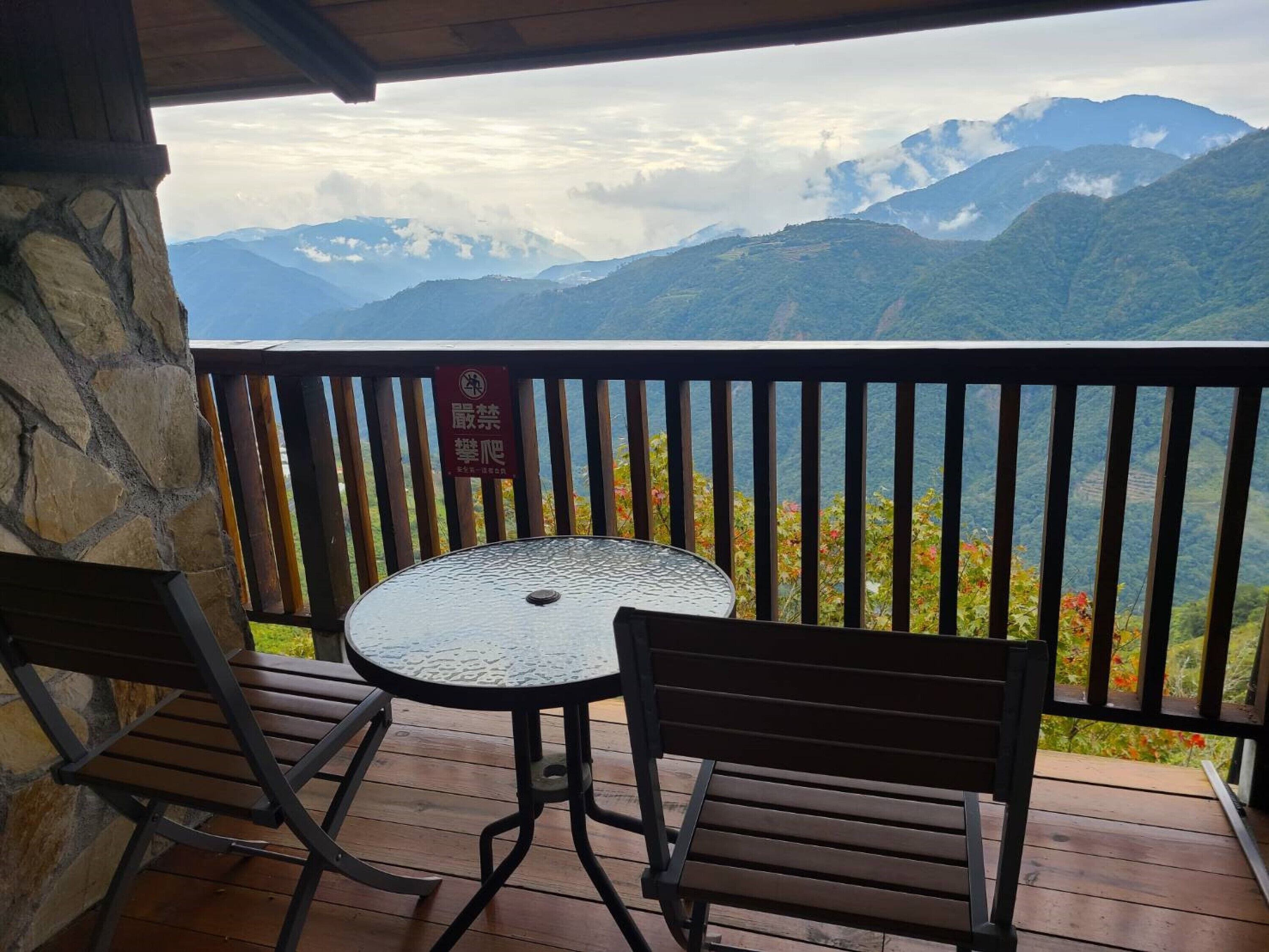 A balcony with a table and chairs, overlooking a mountainous landscape.