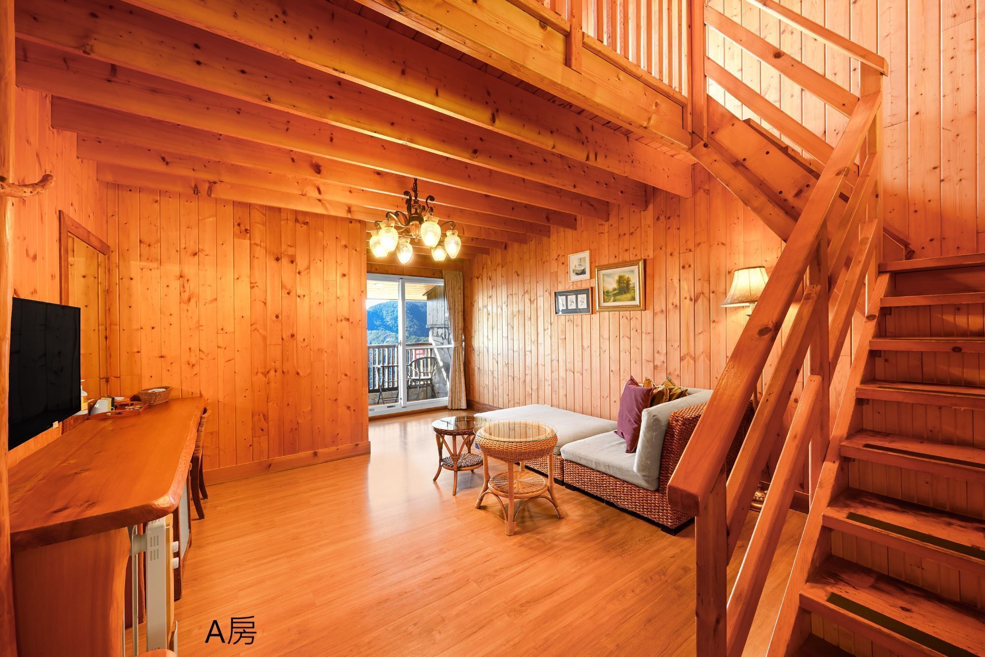 A wooden cabin interior with a sofa, wicker chairs, a TV, and a staircase.