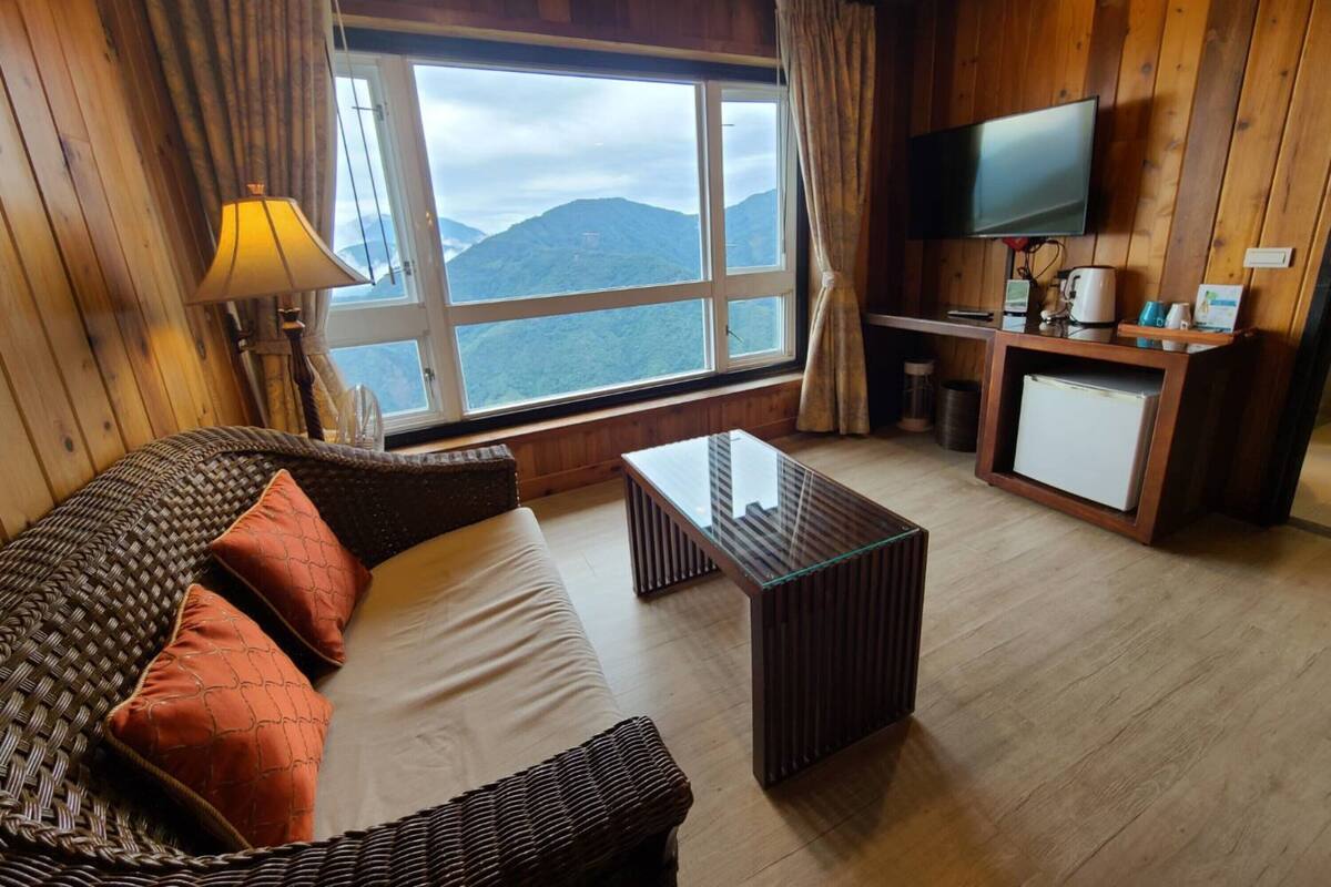 A cozy room with a sofa, a coffee table, a TV, and a window with a mountain view.