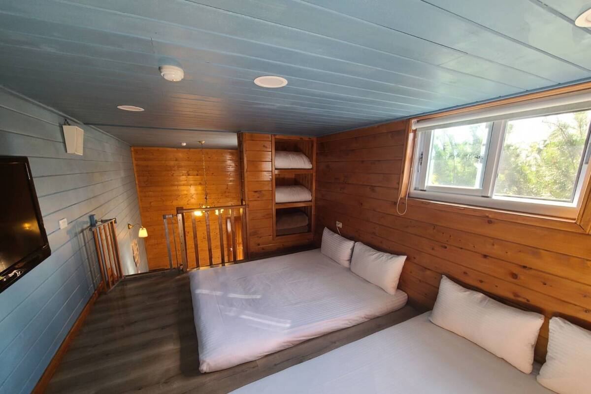 A cabin-style room with two beds, a TV, wooden walls, and a window.