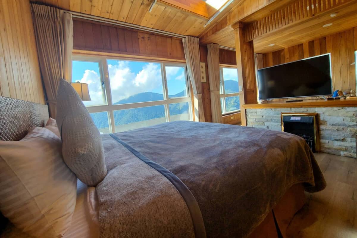 A cozy bedroom with a large bed, a flat-screen TV, and a stone fireplace.