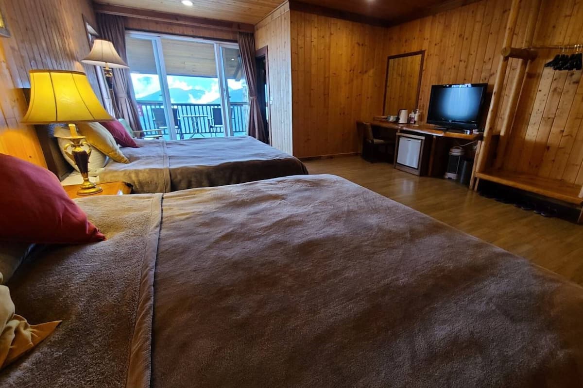 A hotel room with two beds, a TV, a desk, and a balcony with a view.