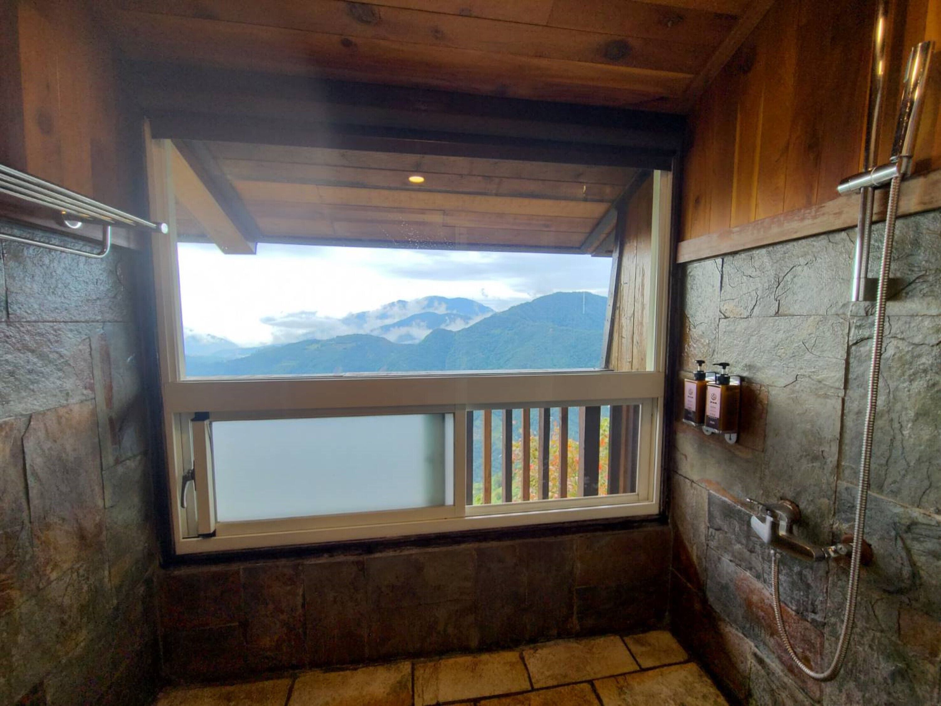 Ein Badezimmer mit Steinwand, Holzboden, einem Fenster mit Bergblick und einer Dusche.