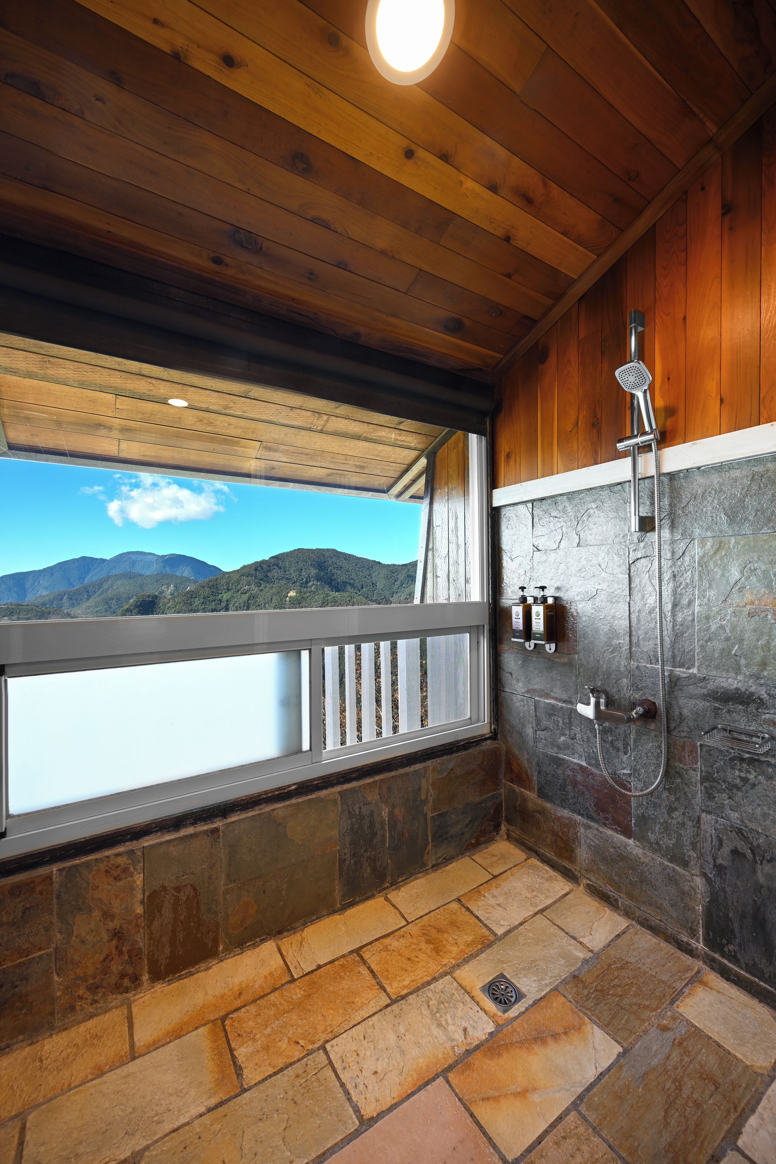A wooden cabin bathroom with a stone floor, a shower, and a view of mountains.