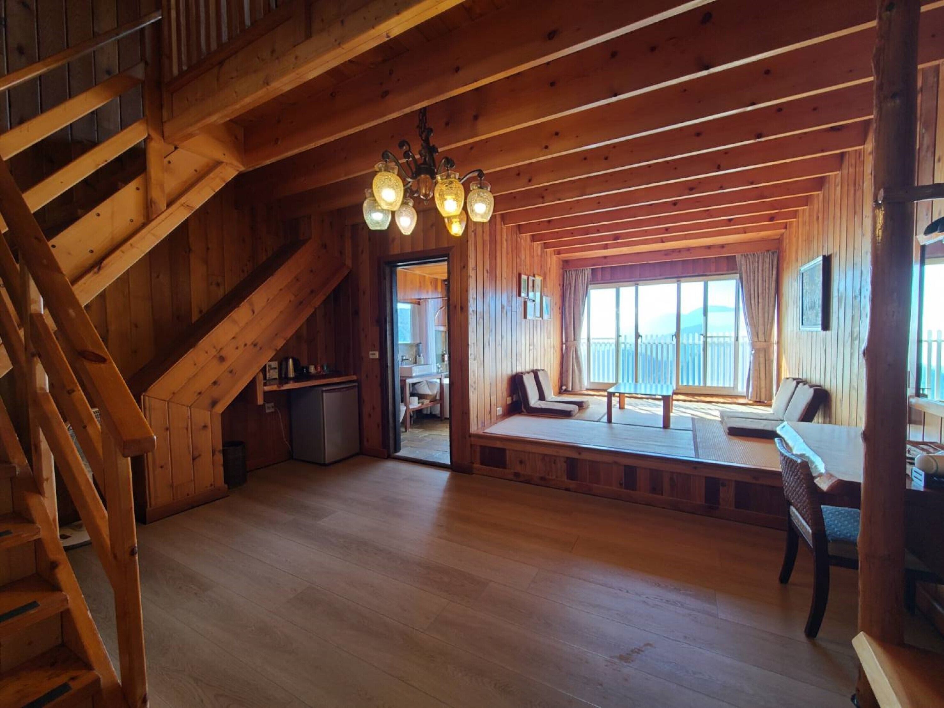 A wooden cabin interior with a staircase, a dining area with a table and chairs, and a kitchen area.