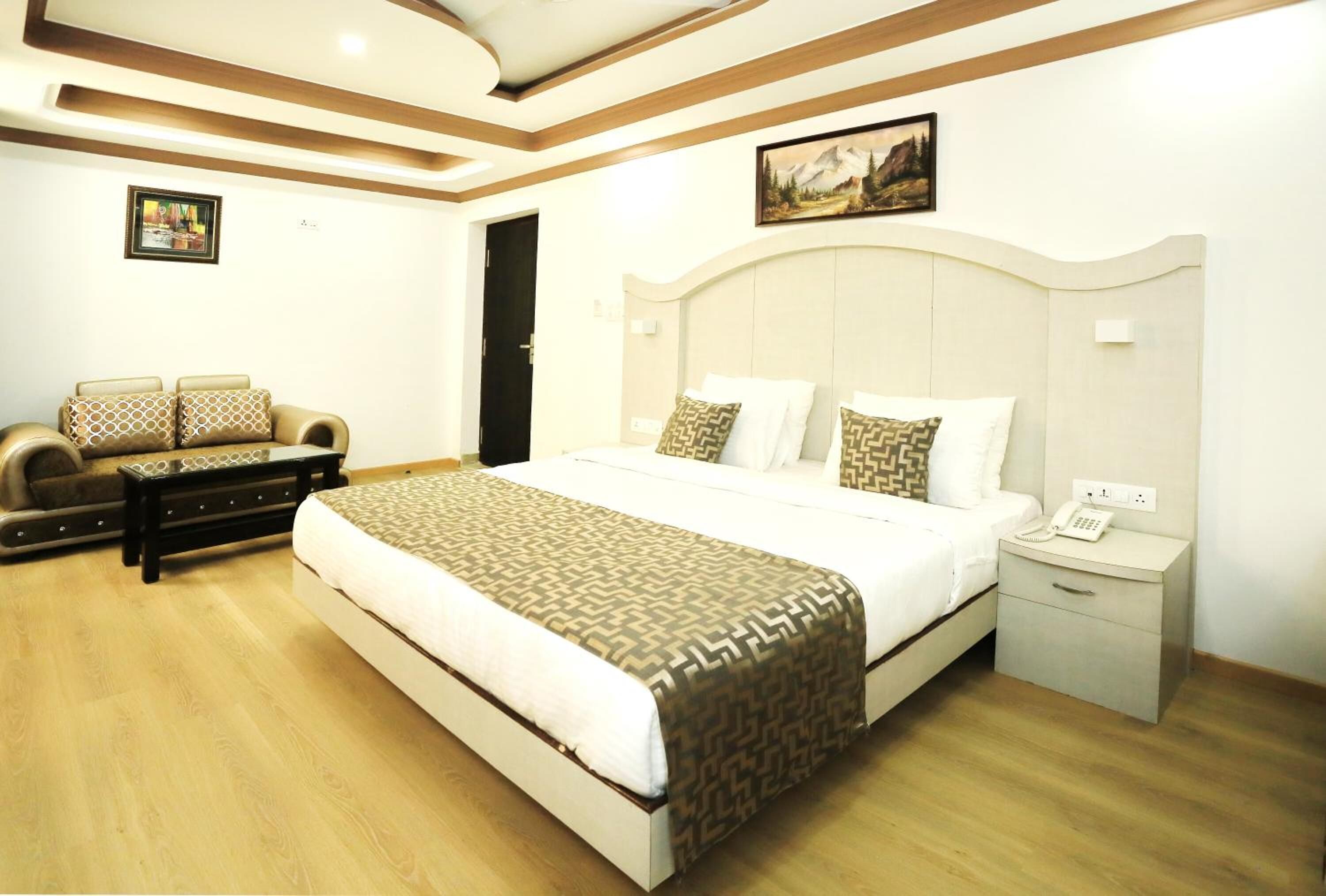 A hotel room with a large bed, a sofa, a bedside table with a phone, and a painting on the wall.