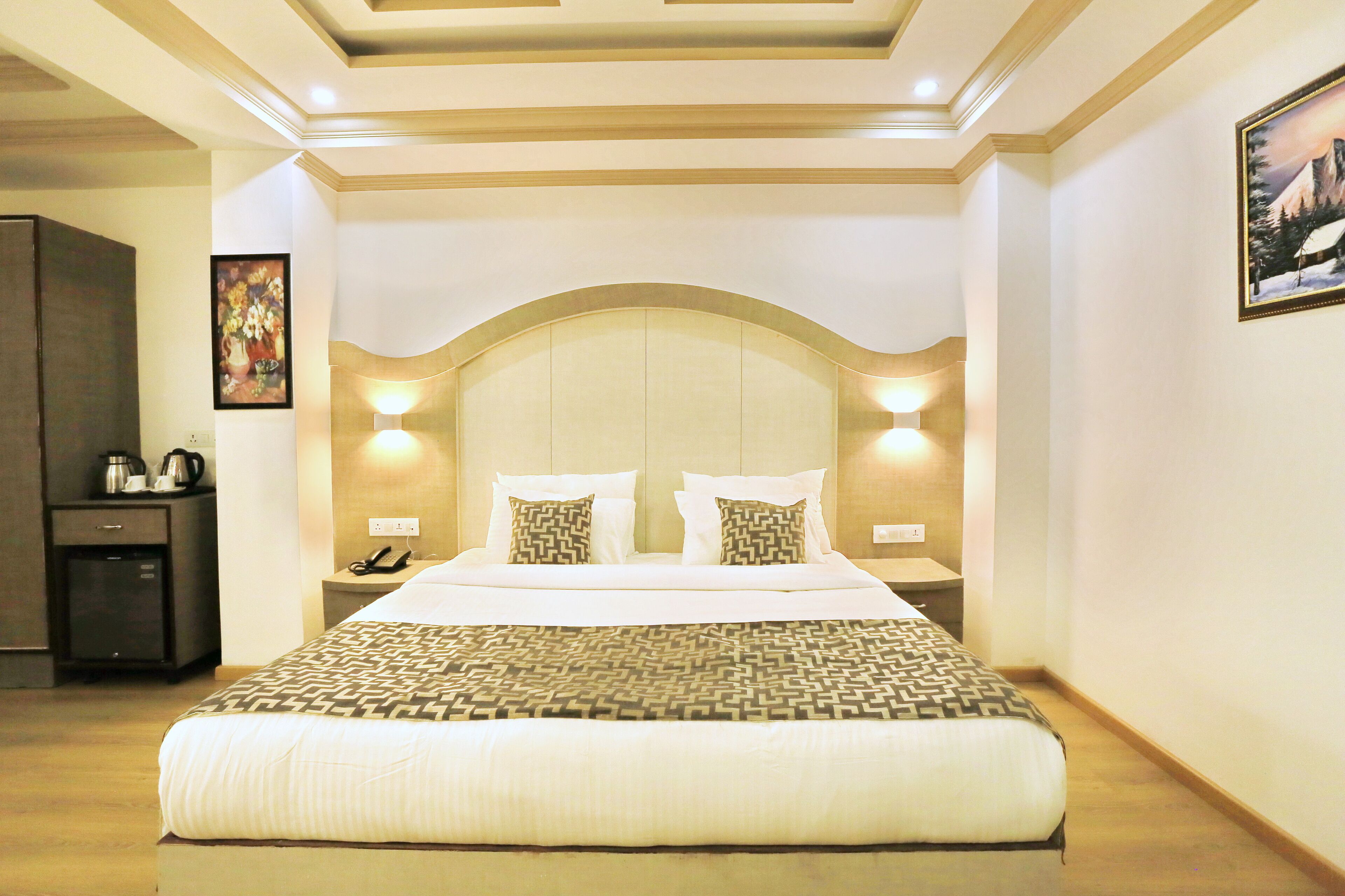 A hotel room with a large bed, bedside tables, a wardrobe, and a painting on the wall.