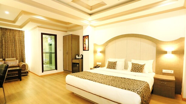 A hotel room with a large bed, a desk with a chair, a wardrobe, and a bathroom with a glass door. - Crown Plaza Residency (Srinagar)