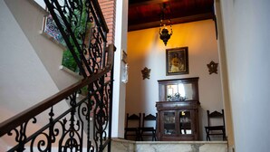 A staircase with ornate black metal railings, a marble landing, and a wooden cabinet with glass doors. - Hotel La Villa (Cervia)
