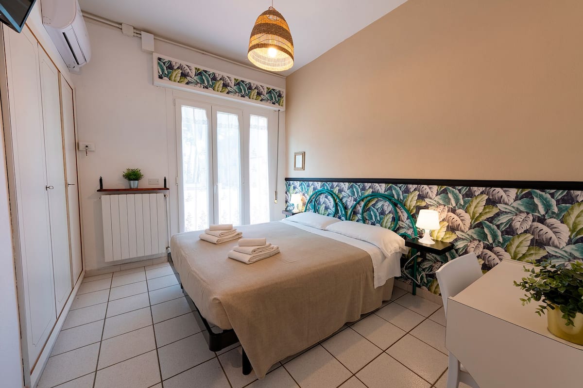 Un dormitorio ordenado con cama, mesita de noche y ventana.