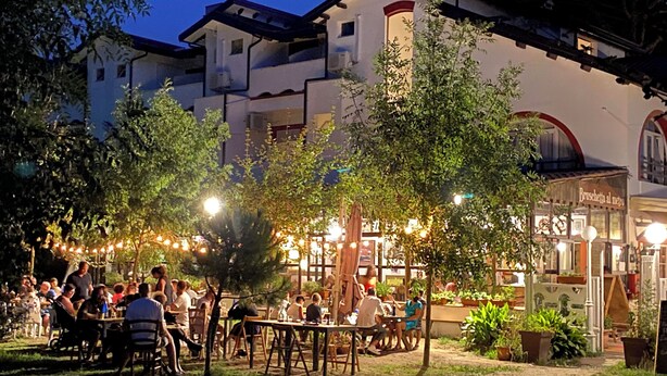 An outdoor dining area with tables and chairs, surrounded by trees and potted plants. - Hotel La Villa (Cervia)