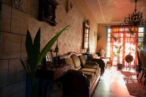 Salón estilo vintage con un sofá, una planta grande, una araña y un tapete estampado.