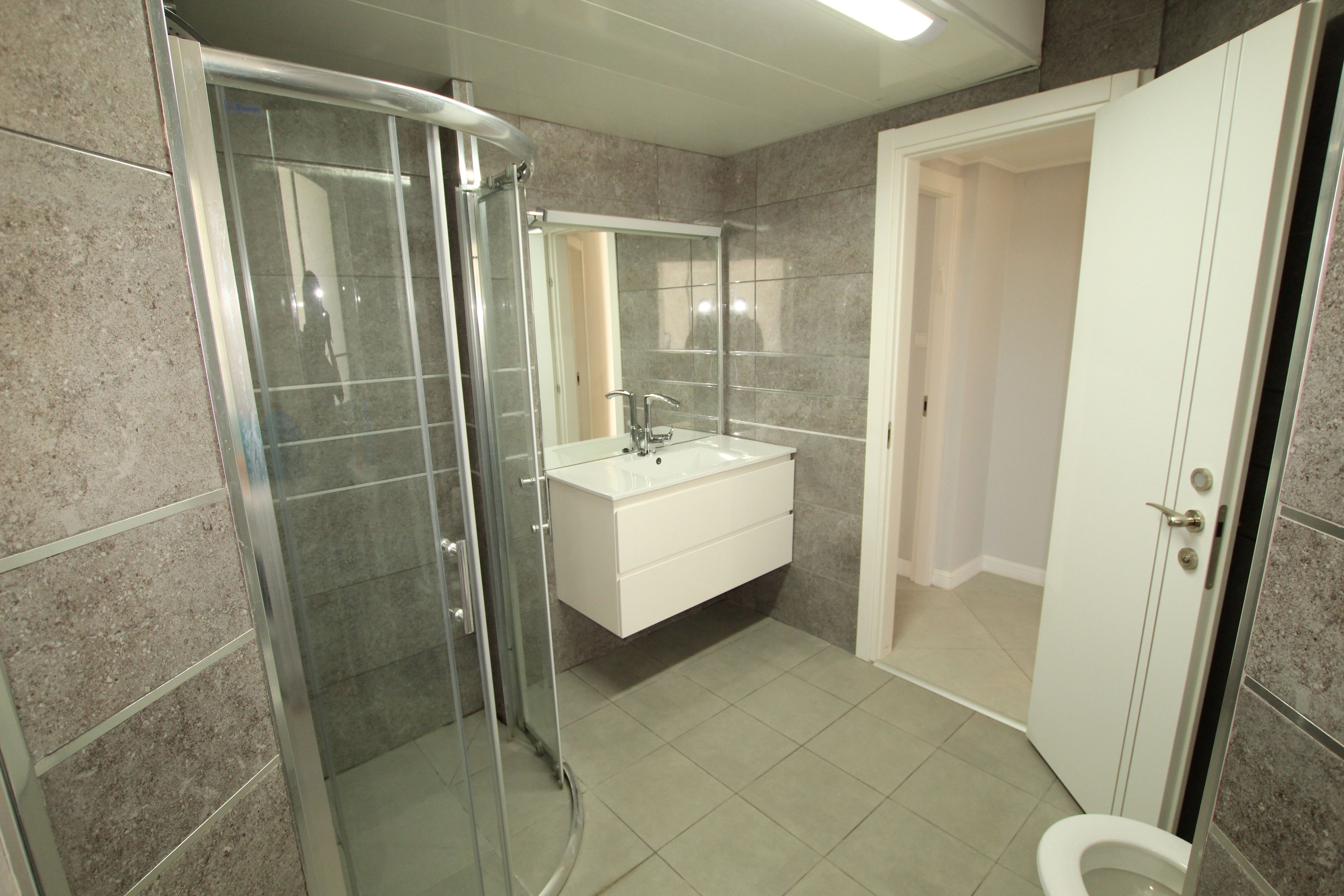 A bathroom with a glass-enclosed shower, a white sink, and a toilet.