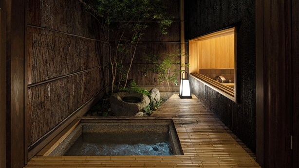 Un interno in stile tradizionale giapponese con pavimento in legno, un piccolo giardino zen e un armadio in legno con una lanterna accesa.