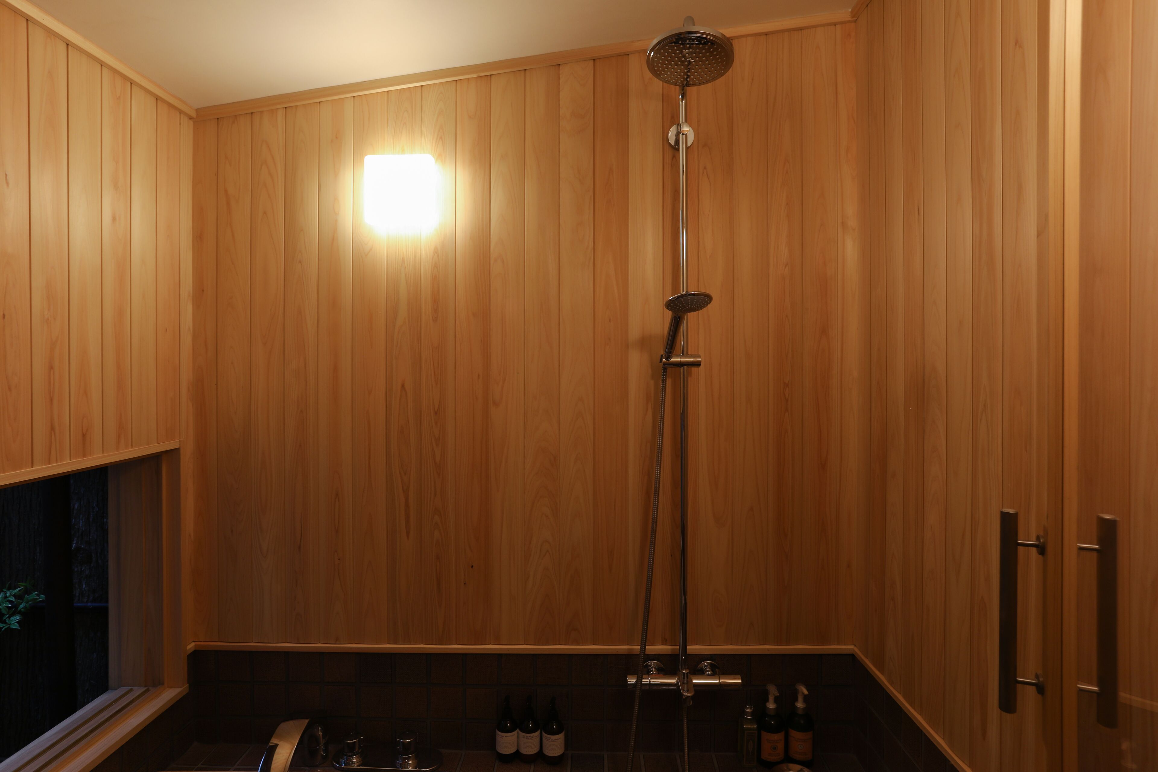 A wooden-paneled bathroom with a shower, a sink, and a bottle of shampoo.