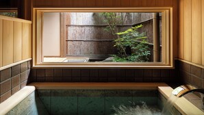 Una tradizionale onsen giapponese con una cornice di legno, una panca in pietra e vista su una pianta di bambù.