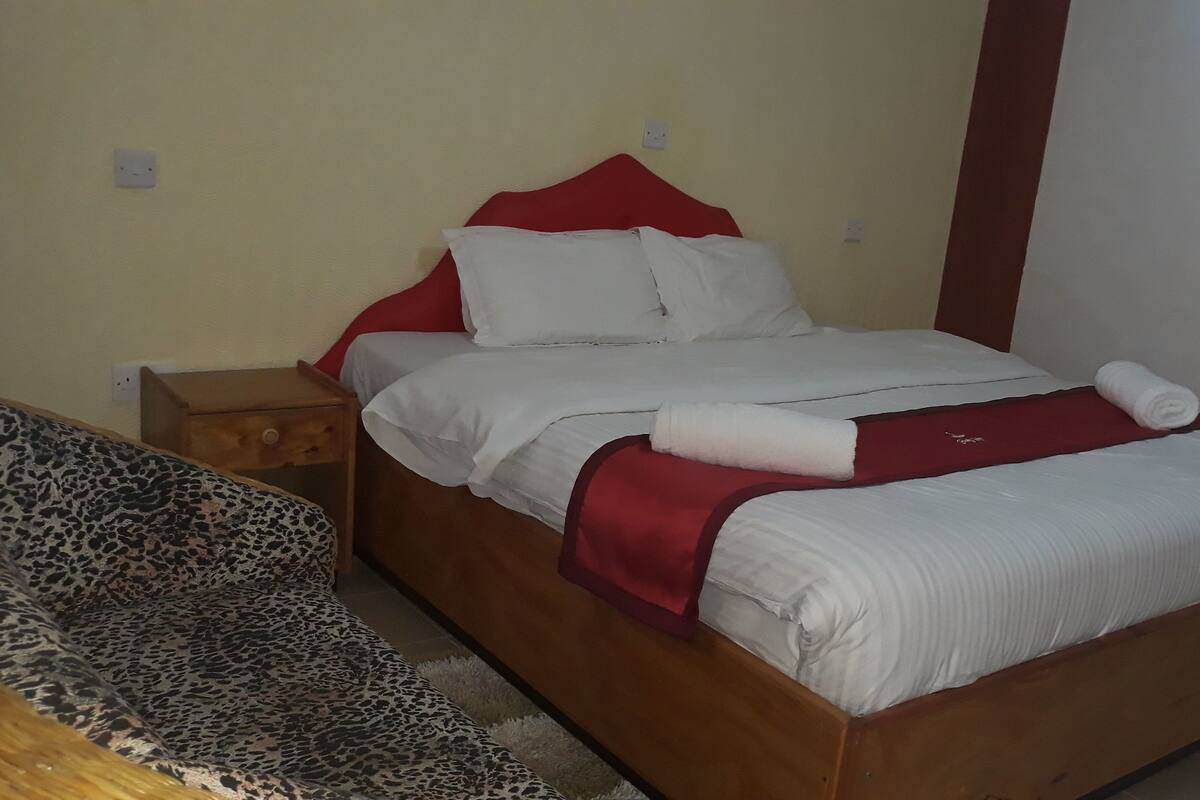 Quarto individual com cama de madeira, roupa de cama branca e cabeceira vermelha.