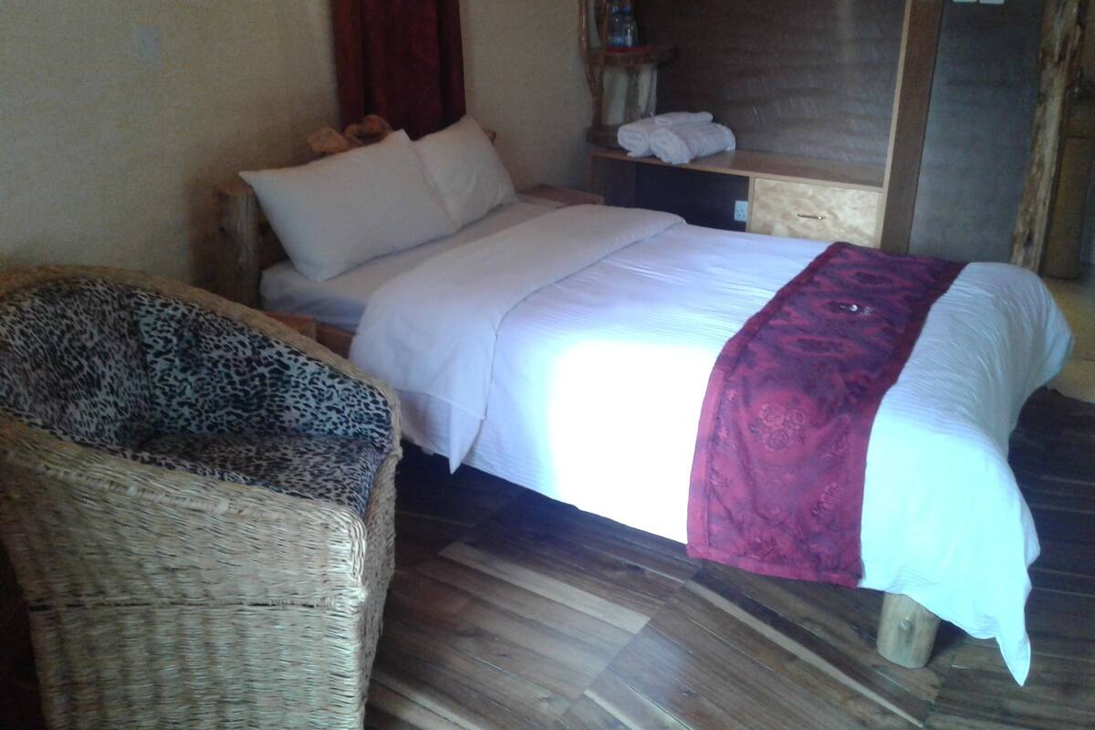 Quarto com uma cama, uma cadeira de vime, uma mesa de cabeceira e um guarda-roupa de madeira.