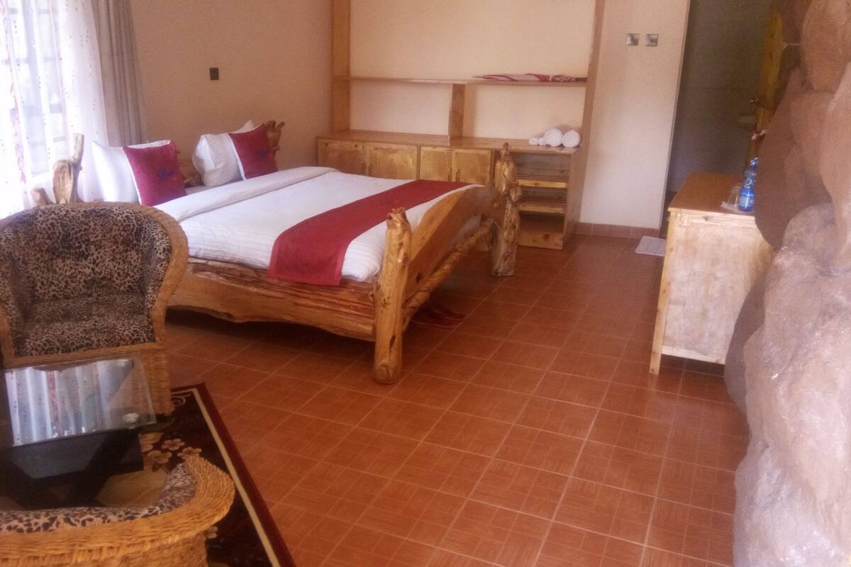 Quarto com cama de madeira, uma cadeira, uma mesinha e um espelho.