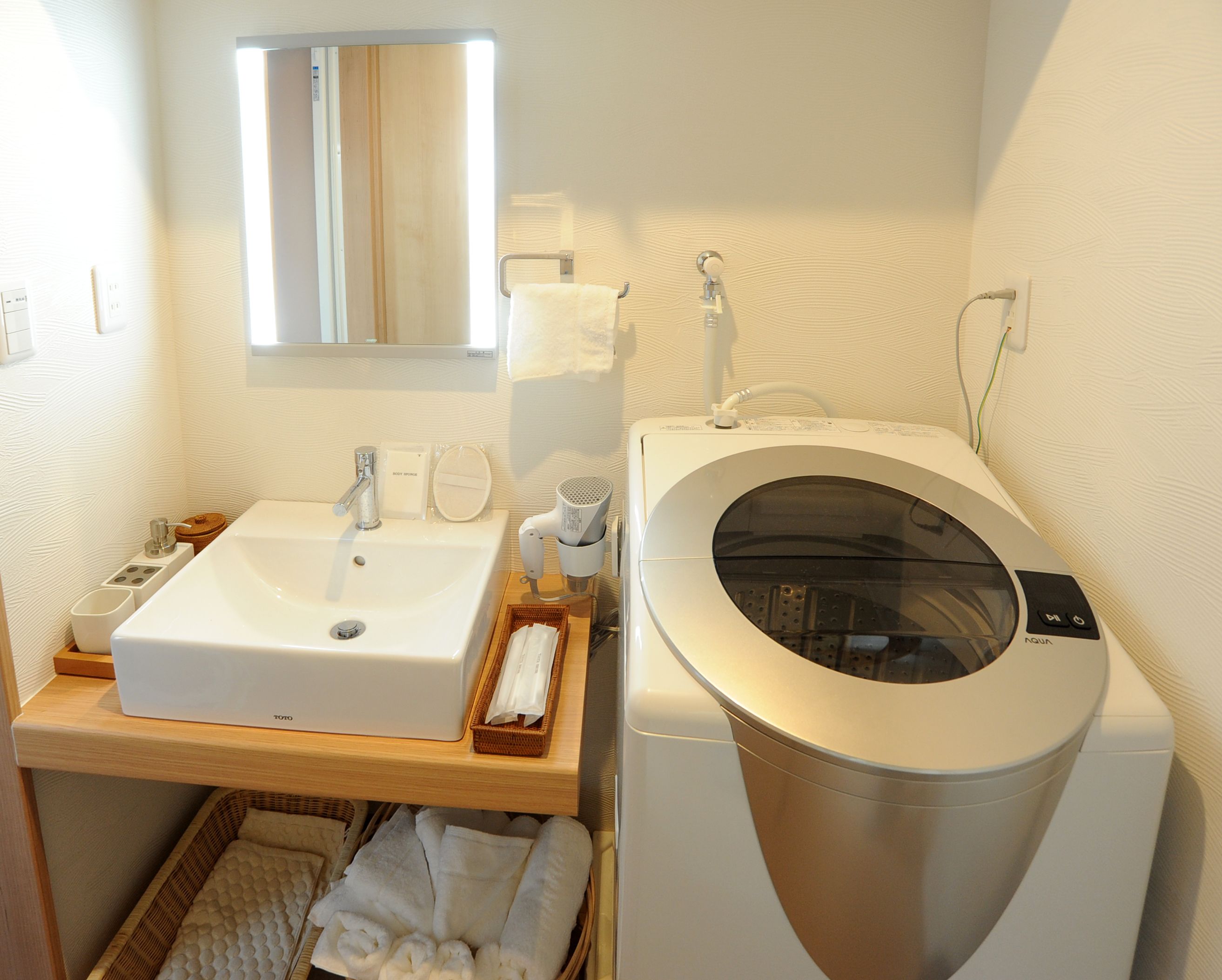 A bathroom with a sink, mirror, towel rack, and a front-loading washing machine.