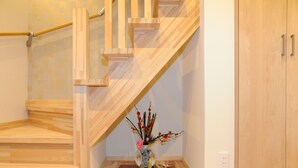 Un escalier en bois avec une rampe, une petite table sur laquelle est posé un vase de fleurs et un meuble en bois.