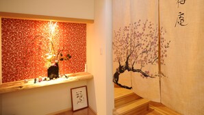 Une pièce de style japonais traditionnel, avec un plafond en bois, un mur décoré de motifs floraux rouges et une porte coulissante ornée d’une peinture représentant des fleurs de cerisier.