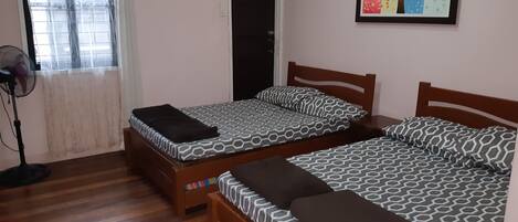 Een kamer met twee bedden, een ventilator, een deur en een raam met gordijn.