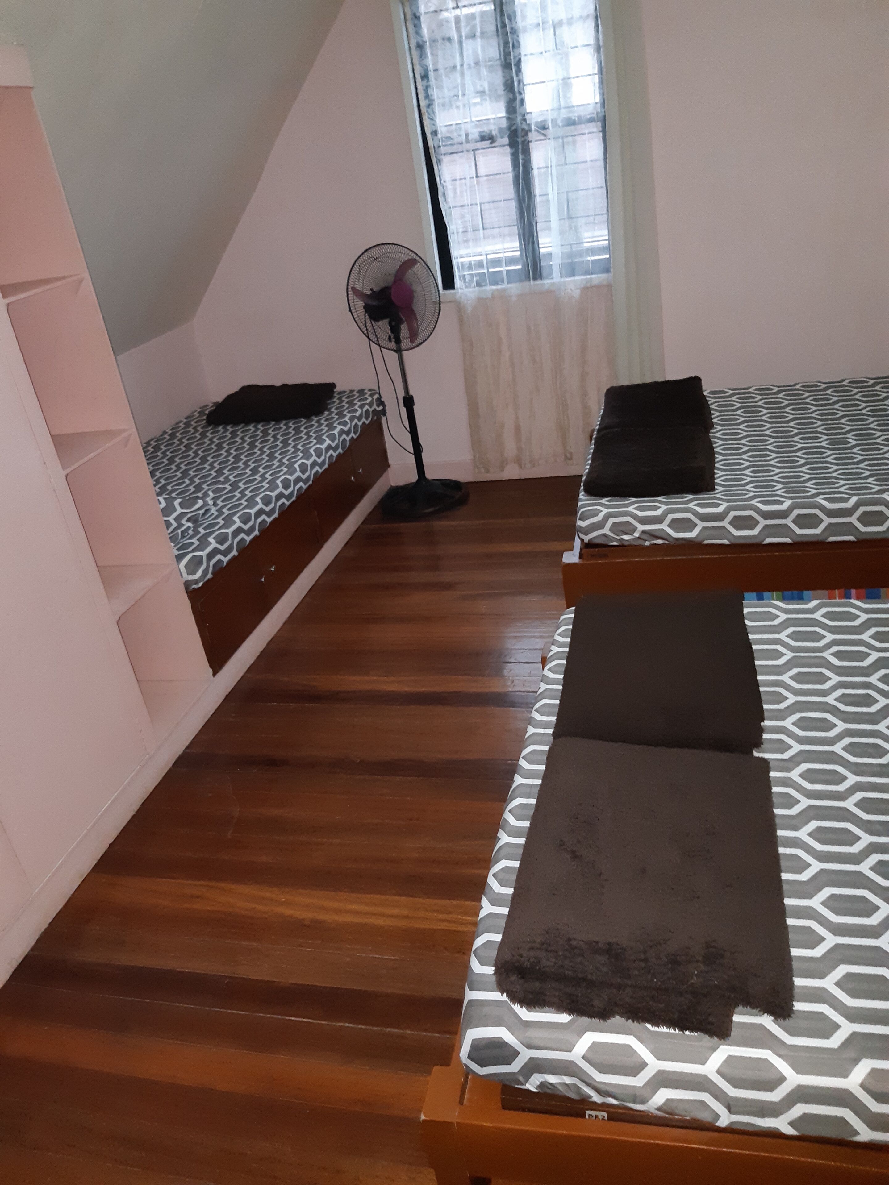 Een kamer met twee bedden, een ventilator en een raam met gordijnen.