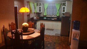 Cocina compacta con mesa, sillas, dispensador de agua y un mueble pequeño.