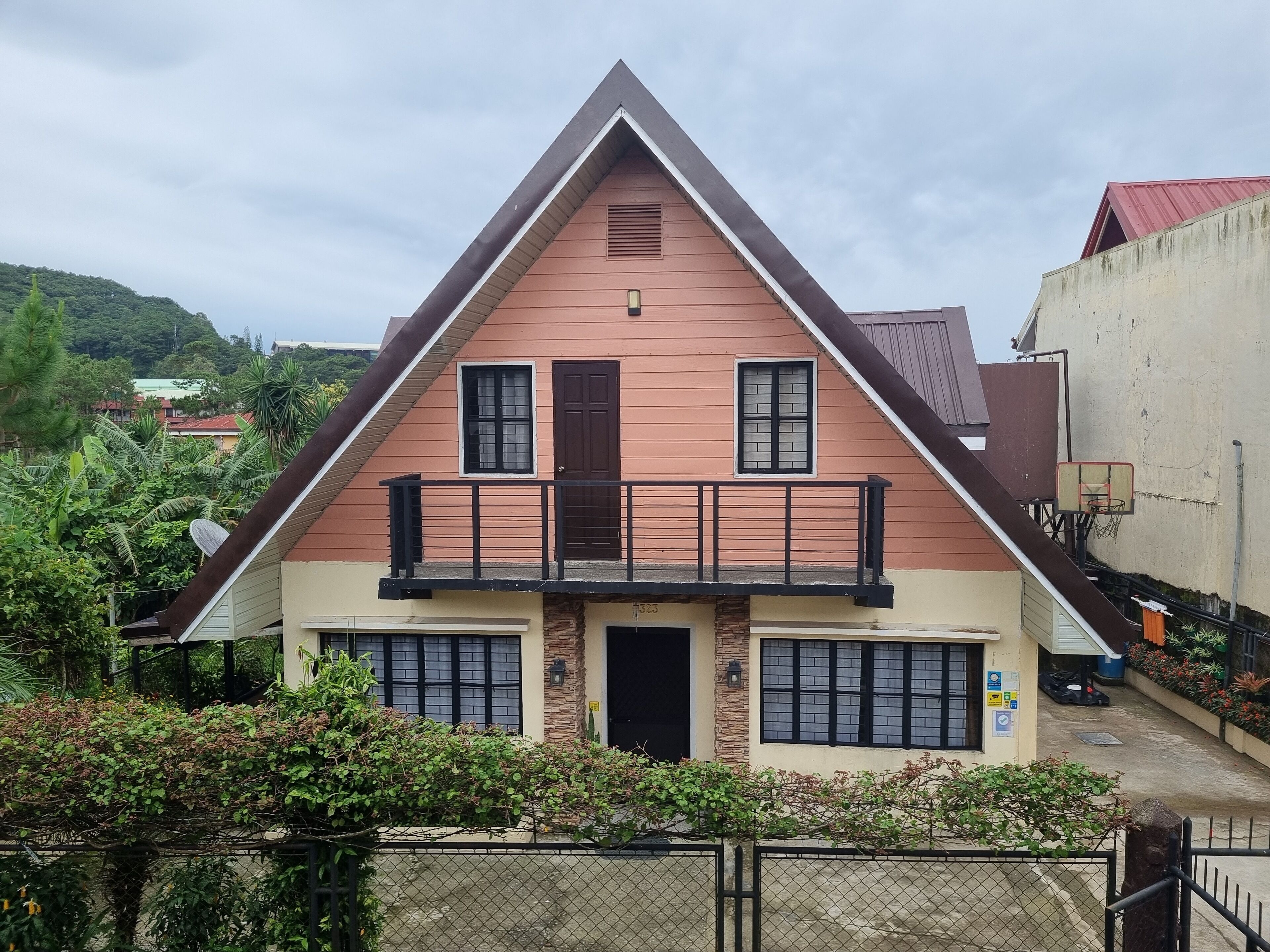 Une maison à deux étages avec un balcon, un panier de basketball et une entrée fermée par un portail.