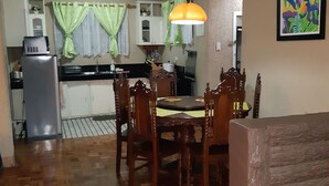 Un comedor con una mesa y sillas de madera, una cocina al fondo y un cuadro de colores en la pared.