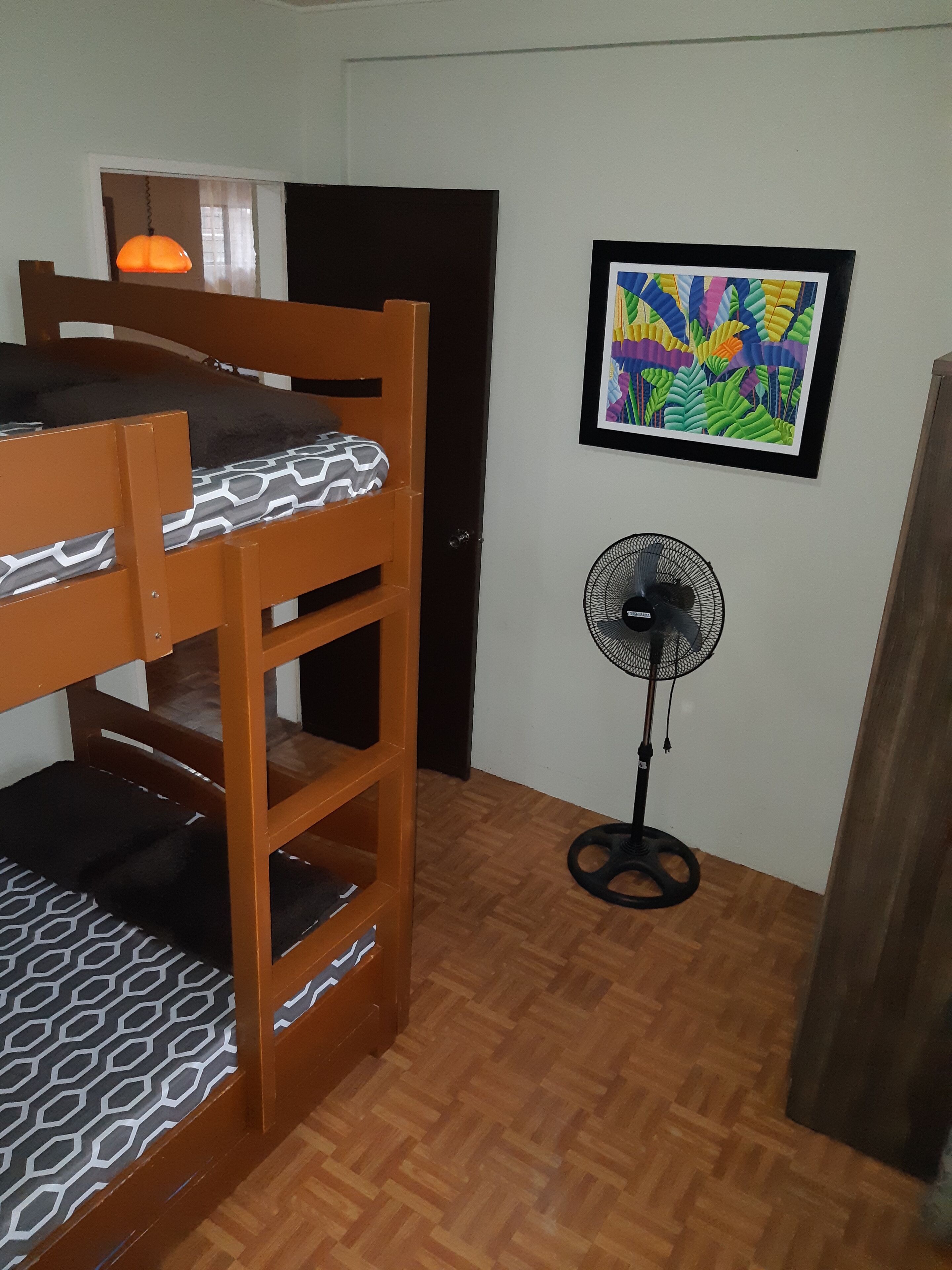 Quarto com beliche, ventilador e uma pintura abstrata colorida na parede.