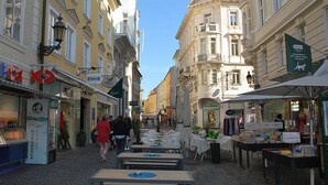 Eine Kopfsteinpflasterstraße gesäumt von Cafés und Geschäften mit Außenbestuhlung und verschiedenen Schaufenstern.