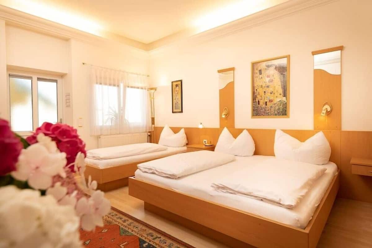 Une chambre d’hôtel avec deux lits, une fenêtre avec des rideaux, un tableau au mur et une porte.