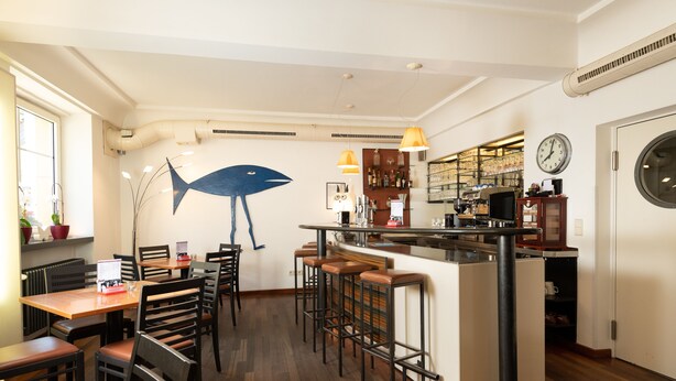 Ein Restaurant mit Barbereich, Holztischen und -stühlen sowie einer großen Wandmalerei mit Fischmotiven.