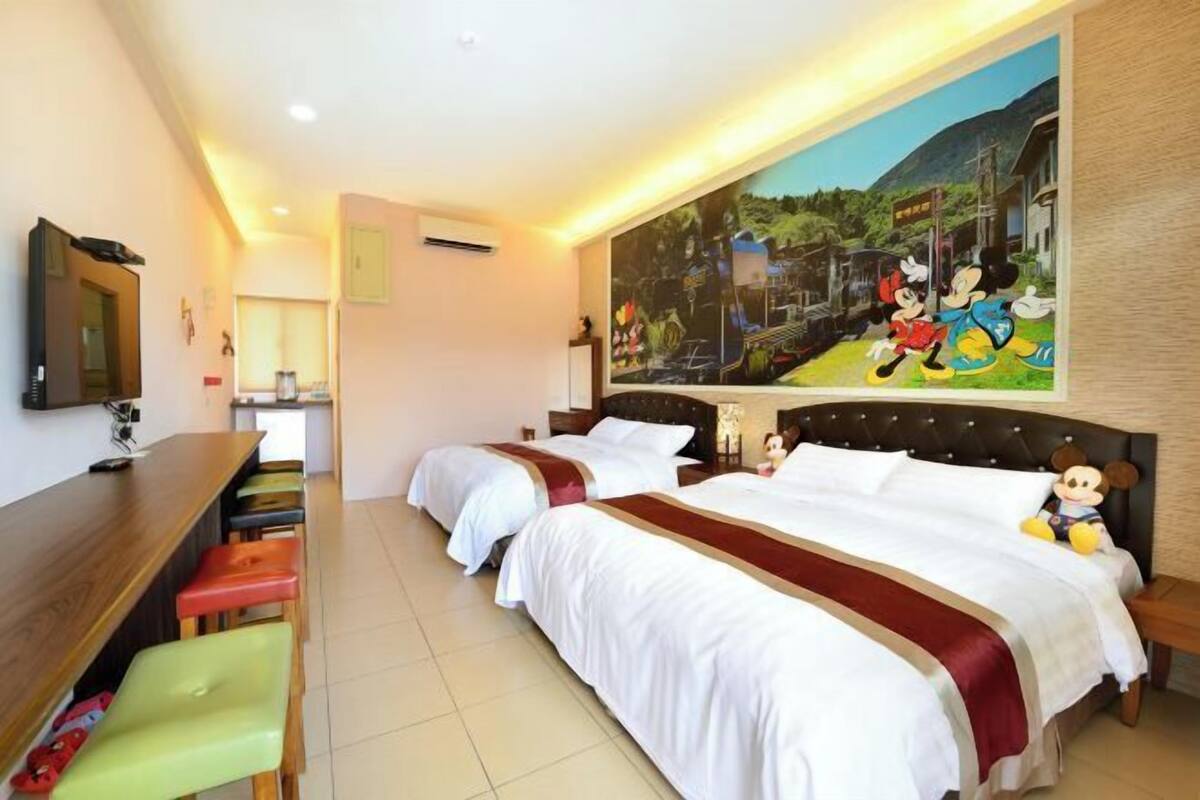 Habitación de hotel con dos camas, un escritorio y un mural de Mickey y Minnie Mouse.
