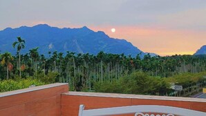 Vista de una cadena montañosa con un atardecer y palmeras al frente.