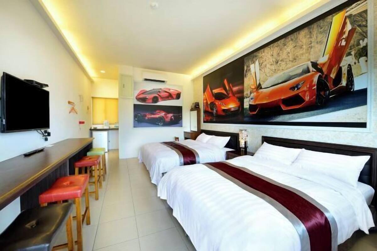 Habitación de hotel con dos camas, un televisor, un escritorio y un mural de coches deportivos.