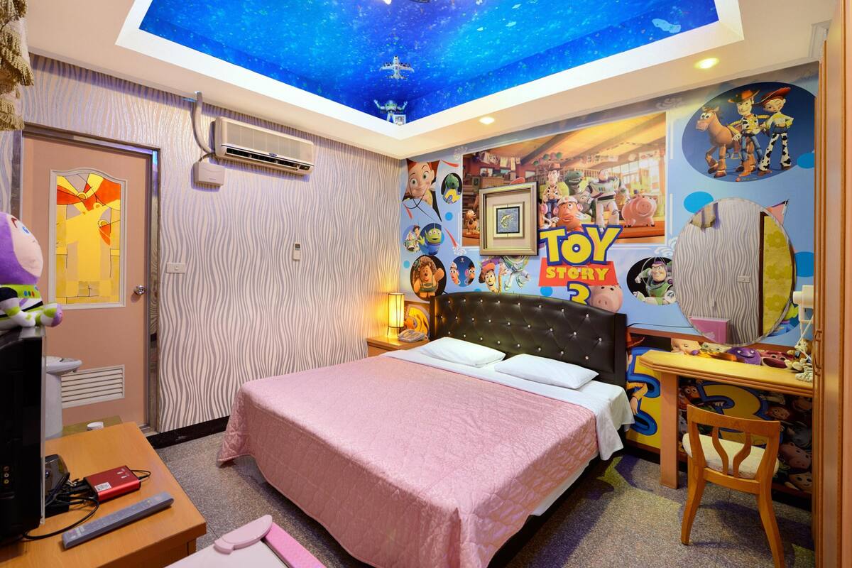 Un dormitorio con una cama, un escritorio y un mural en el techo con personajes de Toy Story.