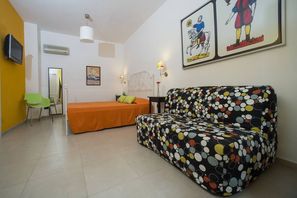 Una stanza con un divano, un letto, una sedia, una TV e opere d'arte alle pareti.