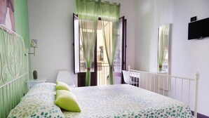 A bedroom with a bed, a nightstand, a chair, a window with curtains, and a balcony visible through the window. - zammu bed and breakfast (Castellammare del Golfo)