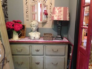 Een antieke dressoir met zes lades, een borstbeeld, een rieten mand, een vaas met bloemen en een lamp met een geruit lampenkap.